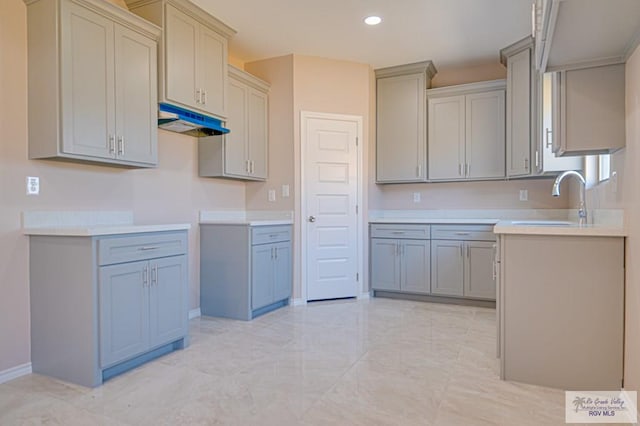 kitchen with baseboards, gray cabinetry, under cabinet range hood, a sink, and recessed lighting