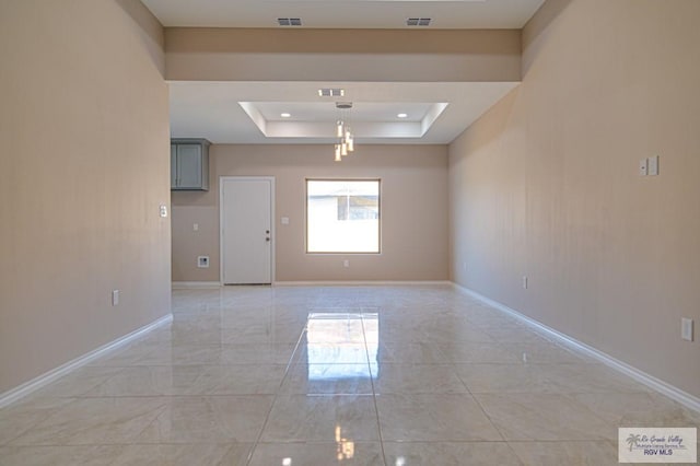 spare room featuring a raised ceiling, visible vents, and baseboards