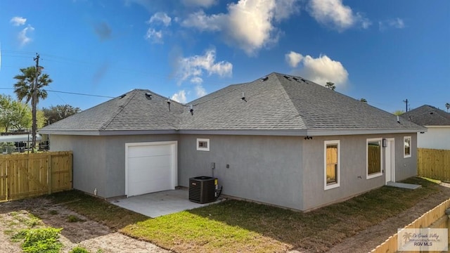 back of house with central air condition unit, stucco siding, a fenced backyard, and roof with shingles