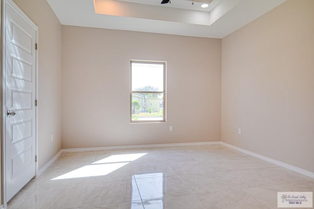 empty room with ceiling fan, a tray ceiling, and baseboards