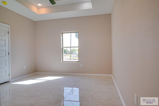 spare room with a ceiling fan, a raised ceiling, and baseboards