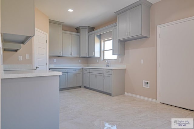 kitchen with baseboards, gray cabinets, light countertops, a sink, and recessed lighting