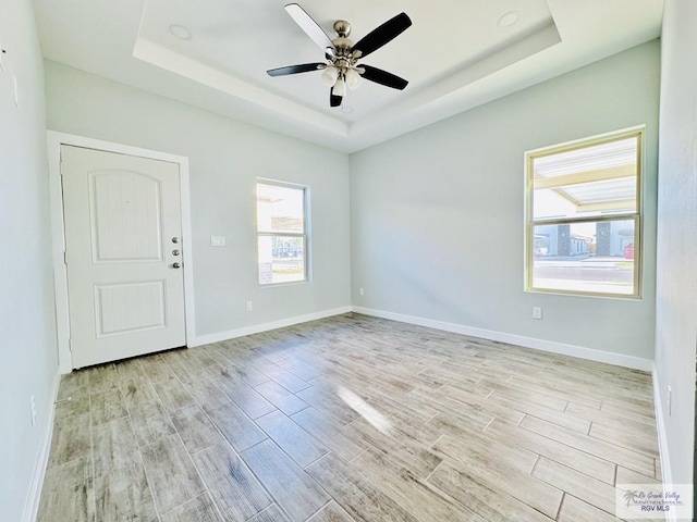 empty room featuring a tray ceiling, light hardwood / wood-style flooring, and ceiling fan