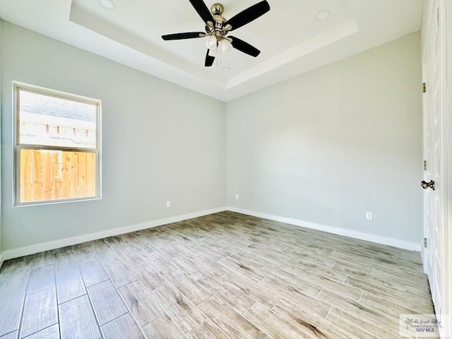 spare room with a tray ceiling, ceiling fan, and light wood-type flooring