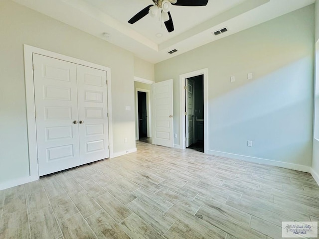 unfurnished bedroom with ceiling fan, light hardwood / wood-style floors, a tray ceiling, and a closet