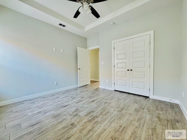 unfurnished bedroom featuring ceiling fan, light hardwood / wood-style floors, a tray ceiling, and a closet