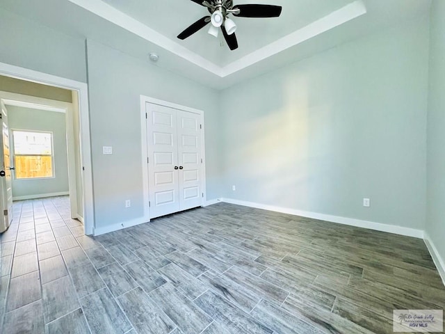 unfurnished bedroom featuring a raised ceiling, a closet, ceiling fan, and hardwood / wood-style floors