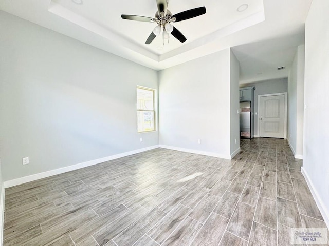 unfurnished room with light hardwood / wood-style flooring, a raised ceiling, and ceiling fan