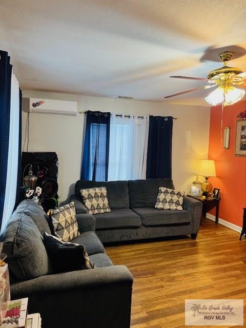 living room featuring wood-type flooring, an AC wall unit, and ceiling fan