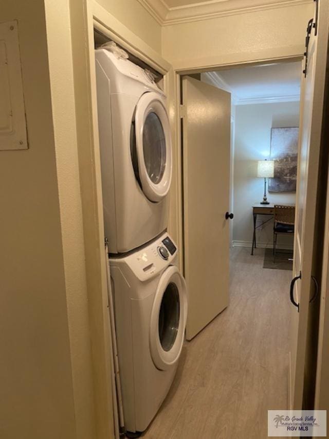 washroom with electric panel, light hardwood / wood-style flooring, a barn door, ornamental molding, and stacked washer / dryer