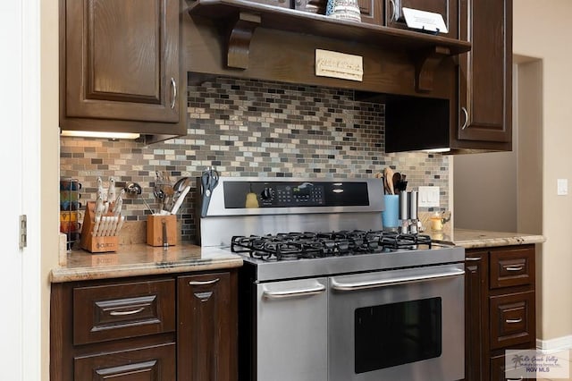 kitchen featuring dark brown cabinets, stainless steel gas range oven, light stone countertops, and backsplash