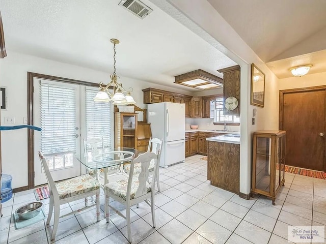 kitchen featuring lofted ceiling, light tile patterned floors, sink, white refrigerator, and decorative light fixtures