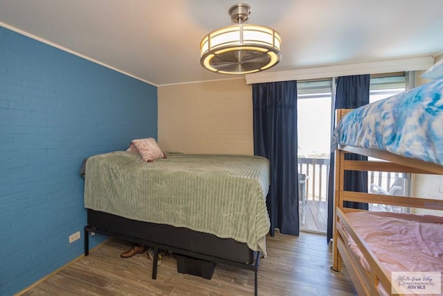 bedroom featuring crown molding, brick wall, and wood finished floors
