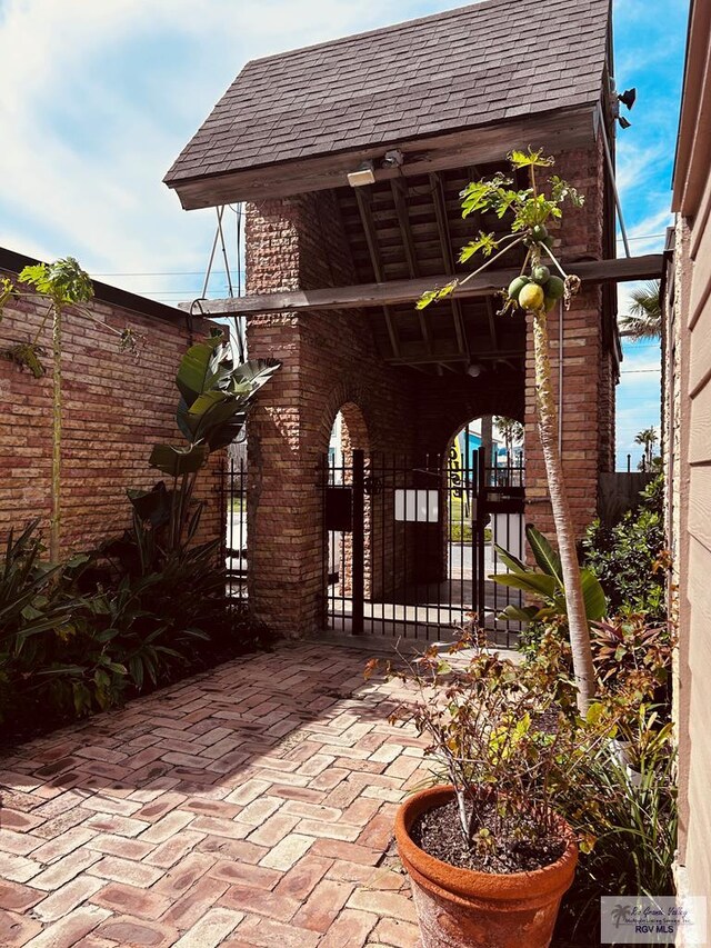 exterior space featuring brick siding, fence, and roof with shingles