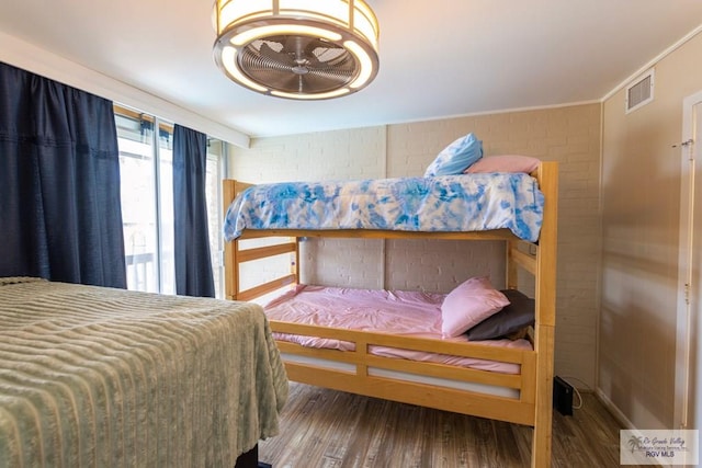 bedroom featuring brick wall, crown molding, visible vents, and wood finished floors
