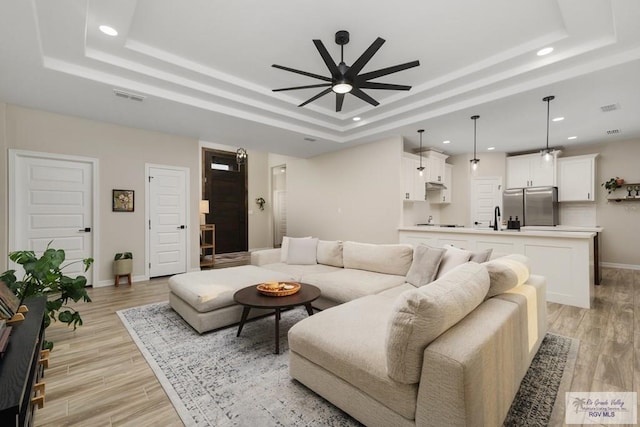 living room with a raised ceiling, ceiling fan, and sink