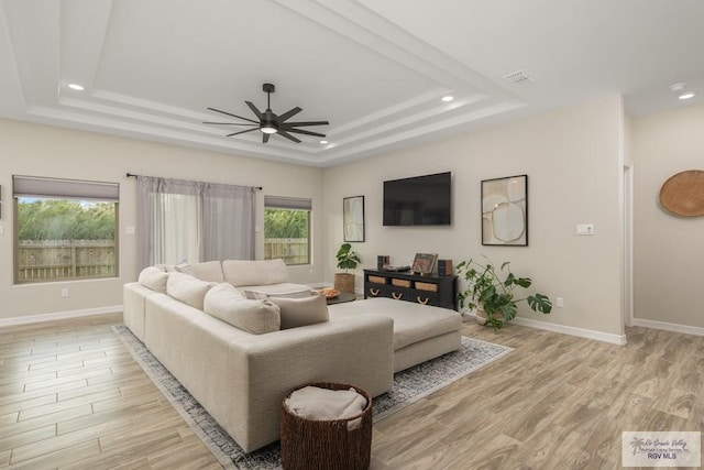 living room with a tray ceiling, ceiling fan, and light hardwood / wood-style flooring