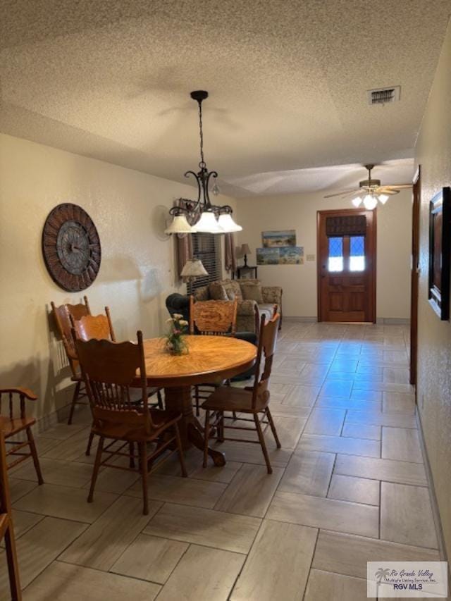 dining space featuring a textured ceiling, ceiling fan with notable chandelier, visible vents, and baseboards
