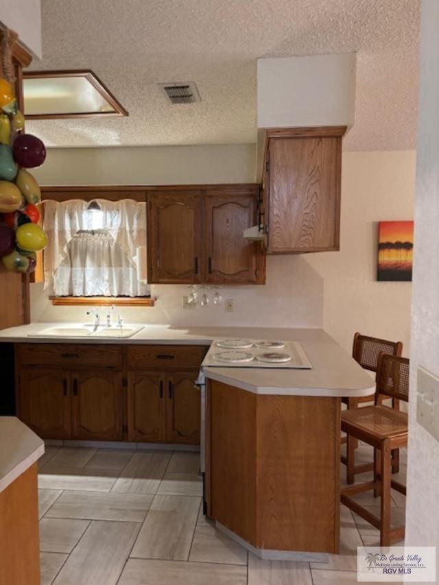 kitchen featuring visible vents, a peninsula, a sink, and light countertops