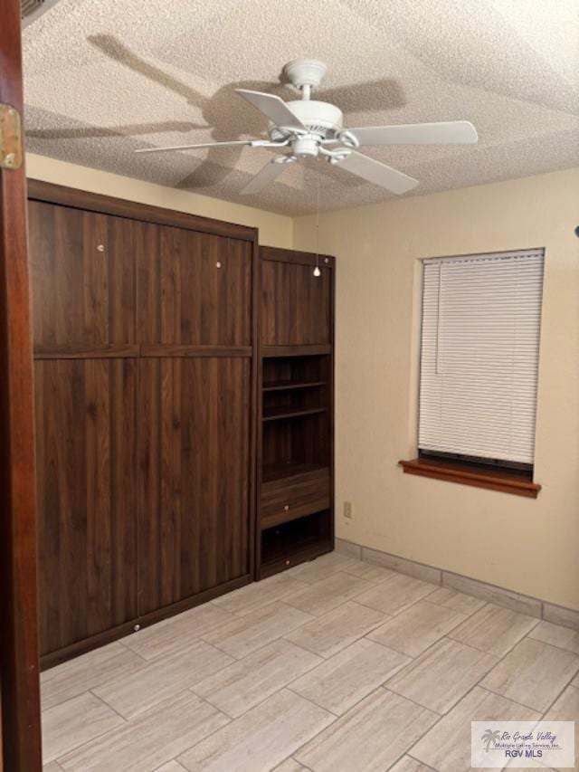 unfurnished bedroom with ceiling fan, baseboards, a textured ceiling, and wood finish floors