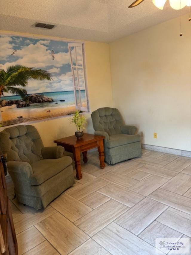 sitting room with baseboards, ceiling fan, visible vents, and a textured ceiling