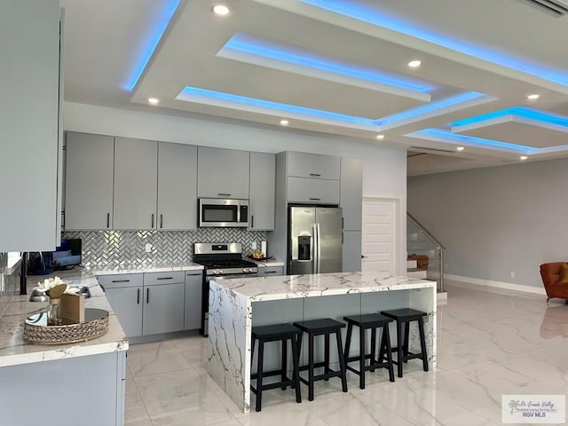 kitchen with appliances with stainless steel finishes, a tray ceiling, marble finish floor, and gray cabinetry