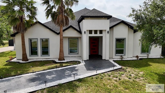 view of front of property featuring roof with shingles, a front lawn, and stucco siding