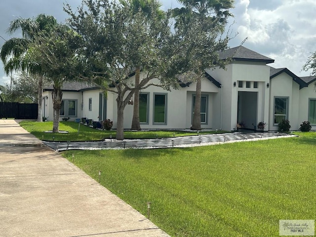 view of front facade featuring a shingled roof, a front lawn, and stucco siding