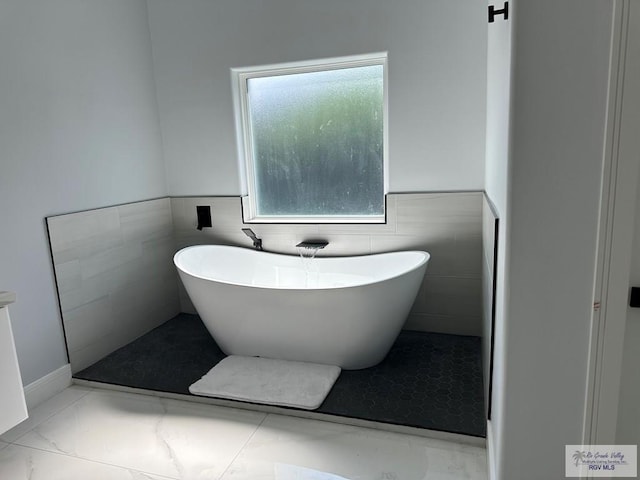 full bathroom with a soaking tub, a wainscoted wall, and marble finish floor