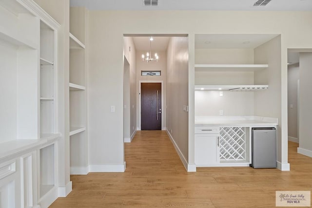 corridor with light hardwood / wood-style flooring, built in features, and a chandelier