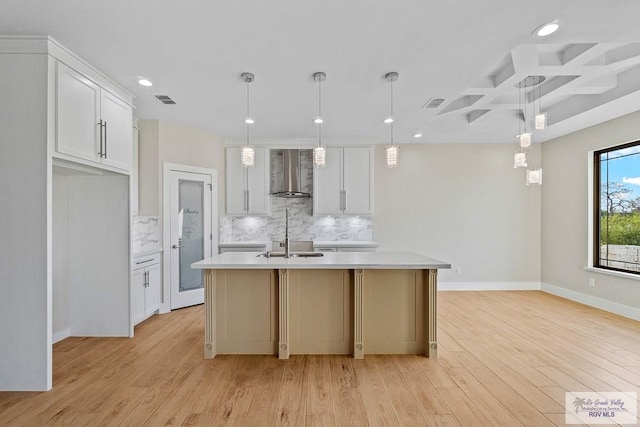 kitchen featuring pendant lighting, wall chimney exhaust hood, and a center island with sink