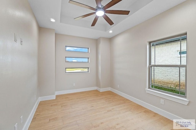 spare room featuring light hardwood / wood-style flooring, ceiling fan, and a tray ceiling