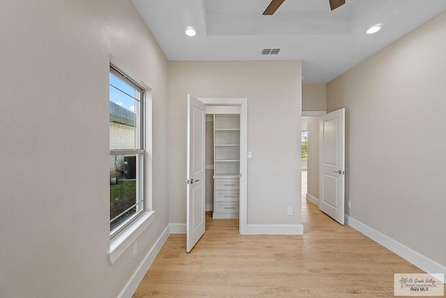 unfurnished bedroom featuring a spacious closet, a tray ceiling, a closet, ceiling fan, and light hardwood / wood-style floors