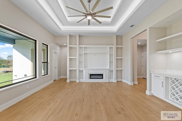 unfurnished living room with a tray ceiling, light hardwood / wood-style flooring, built in features, and ceiling fan