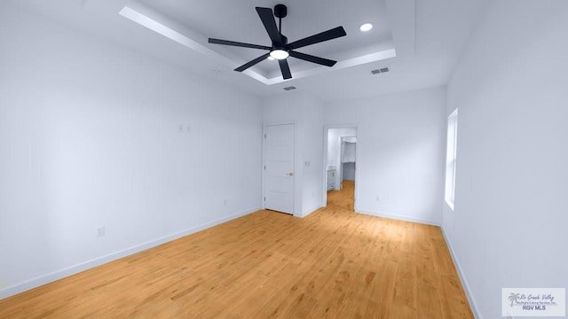 unfurnished bedroom with ceiling fan, a tray ceiling, and light hardwood / wood-style flooring