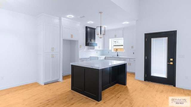 kitchen featuring sink, a center island, light hardwood / wood-style floors, white cabinets, and decorative light fixtures