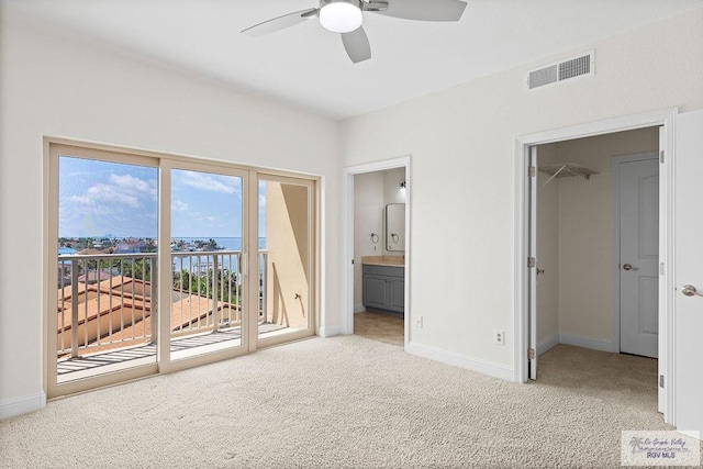 unfurnished bedroom featuring a walk in closet, ensuite bathroom, access to outside, light colored carpet, and a closet