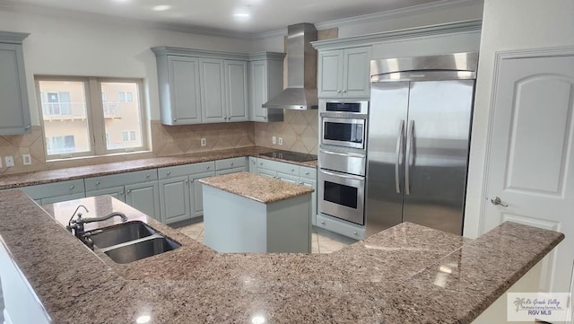 kitchen featuring a center island, wall chimney exhaust hood, stainless steel appliances, sink, and ornamental molding