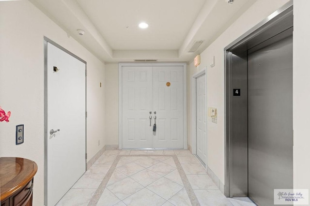 hallway with light tile patterned floors, elevator, and a tray ceiling