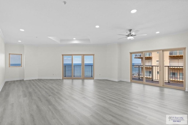 spare room with ceiling fan, light wood-type flooring, and a tray ceiling