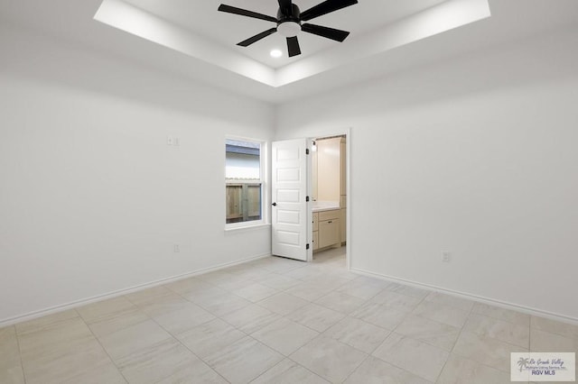 unfurnished bedroom featuring ceiling fan, connected bathroom, and a tray ceiling