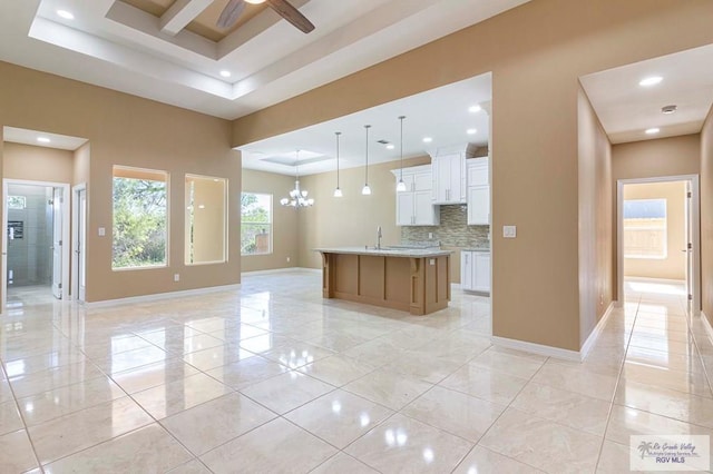 kitchen featuring pendant lighting, a tray ceiling, a kitchen island with sink, white cabinets, and ceiling fan with notable chandelier