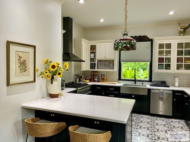 kitchen with white cabinets, wall chimney exhaust hood, appliances with stainless steel finishes, tasteful backsplash, and kitchen peninsula