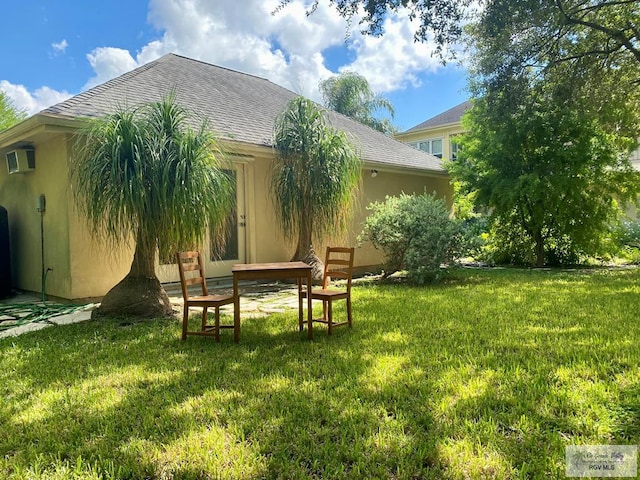 rear view of property with a shingled roof, a wall mounted air conditioner, and a yard