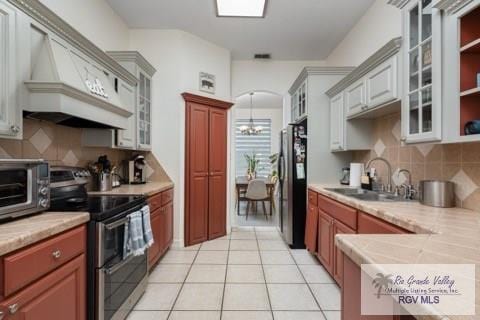 kitchen featuring sink, appliances with stainless steel finishes, white cabinetry, light tile patterned flooring, and custom exhaust hood