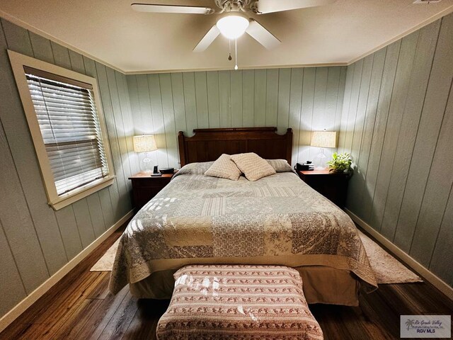 bedroom with dark hardwood / wood-style floors, wood walls, ornamental molding, and ceiling fan