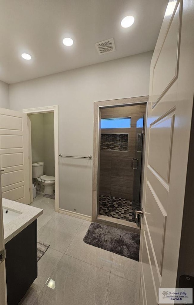 bathroom featuring tile patterned flooring, vanity, a shower with shower door, and toilet