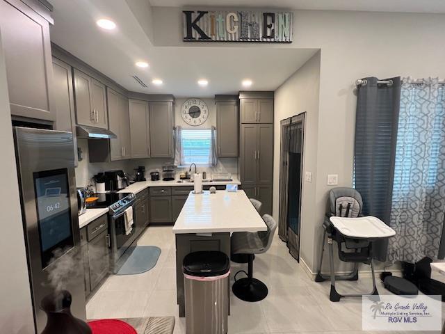 kitchen with under cabinet range hood, light countertops, gray cabinets, stainless steel fridge, and black / electric stove