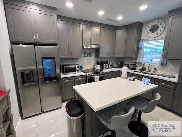 kitchen with gray cabinetry, sink, a center island, stainless steel appliances, and a kitchen bar