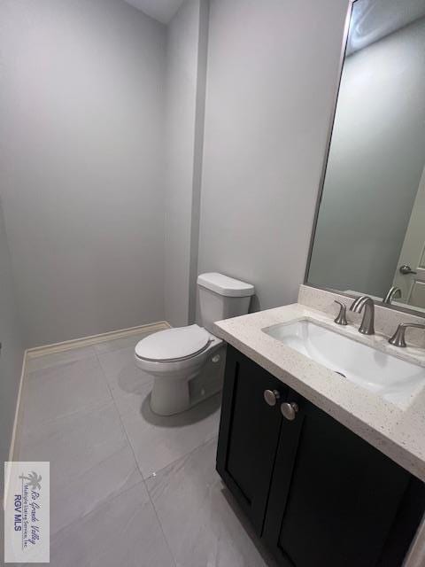 half bathroom with vanity, toilet, baseboards, and tile patterned flooring